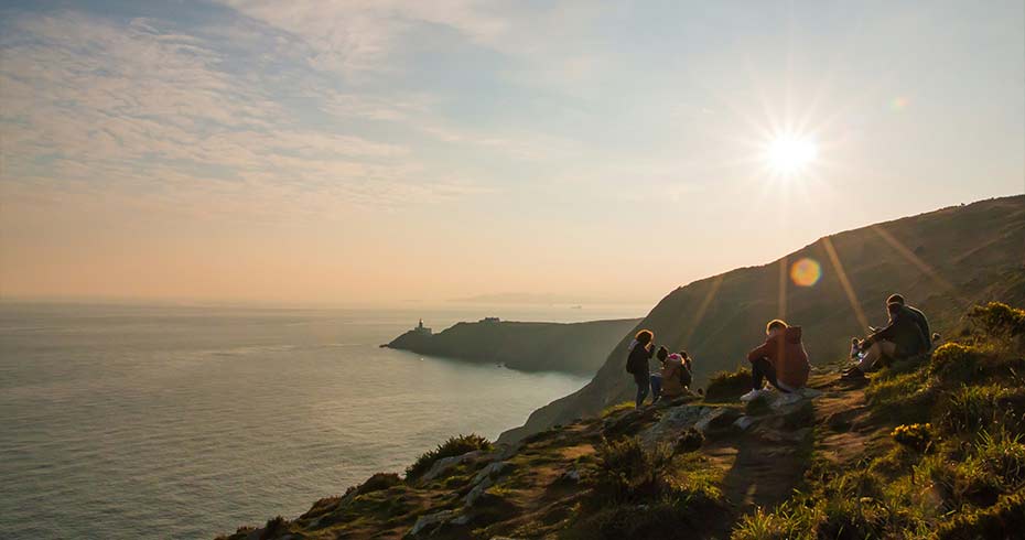 People rest on the Howth Cliff Walk overlooking Dublin Bay at sunset, one of the most popular coastal hikes near Dublin.